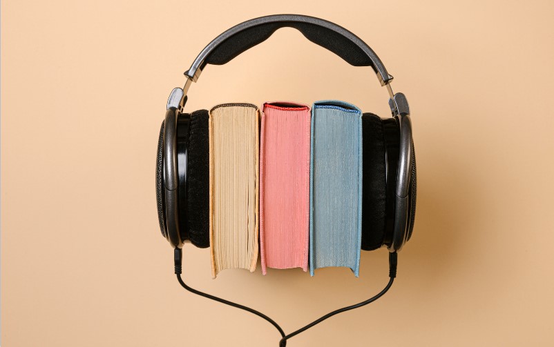 Un casque audio entoure trois livres posés debout : le livre s'écoute aussi.